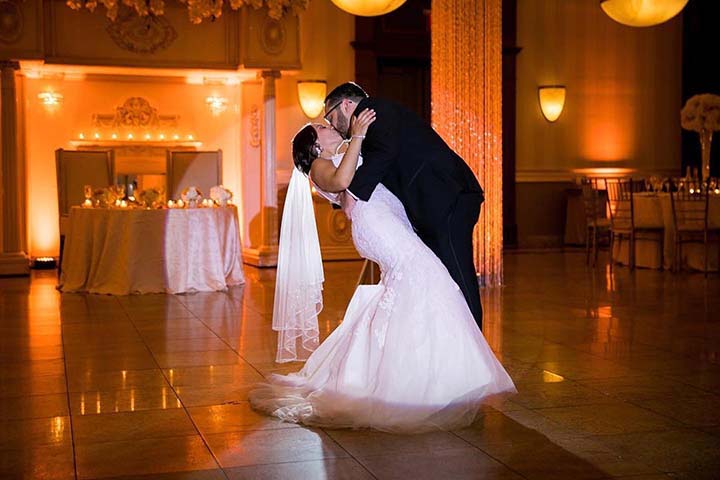 Bride and groom sharing a romantic first dance in a warm candlelit wedding venue.
